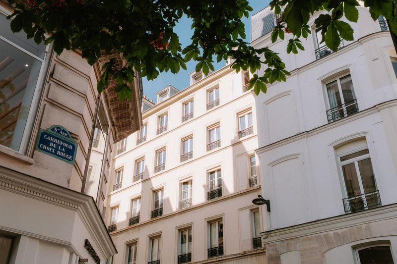 Street view of elegant Parisian buildings at Carrefour de la Croix Rouge with lush greenery overhead.