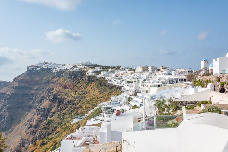 Explore the stunning white architecture on Santorini's cliffside under a bright blue sky.