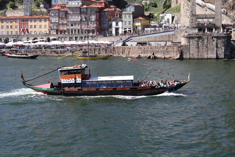 A traditional boat cruises on the Douro River with colorful Porto buildings in the background.