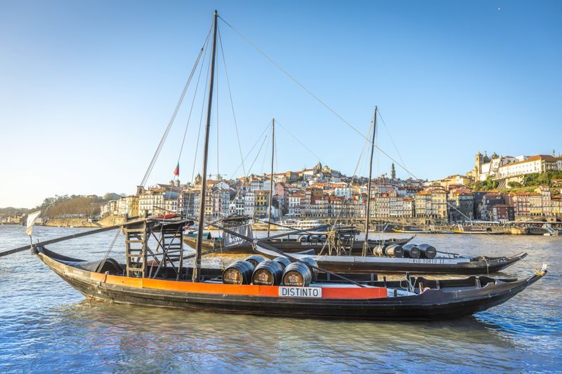 Rabelo boats with wine barrels on the Douro River, Porto showcasing historic waterfront architecture.