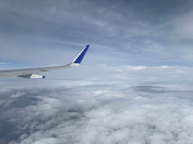 A stunning aerial view from an airplane with a blue wingtip soaring above fluffy white clouds.