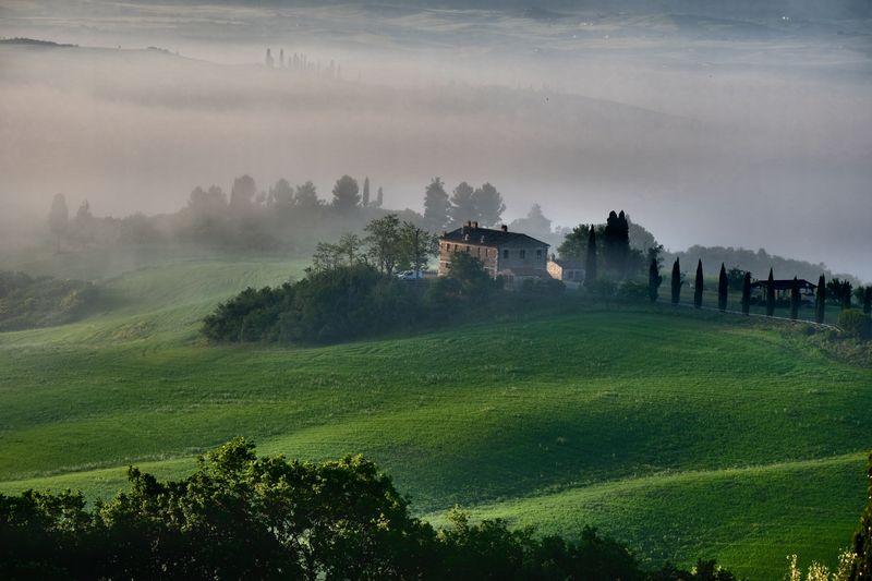 Serene misty landscape in Tuscany with rolling hills and a farmhouse.