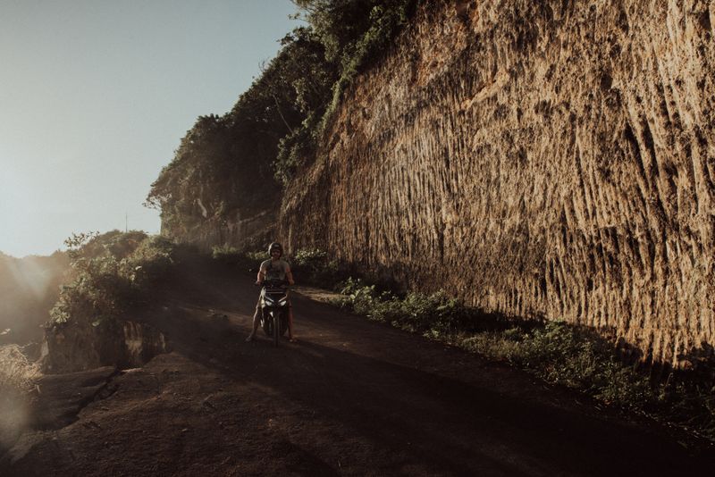 Explore Bali's rugged landscapes on a motor scooter along a dirt road at sunset.