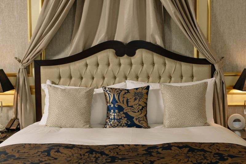 Elegant hotel room with plush headboard, decorative pillows, and luxurious curtains.