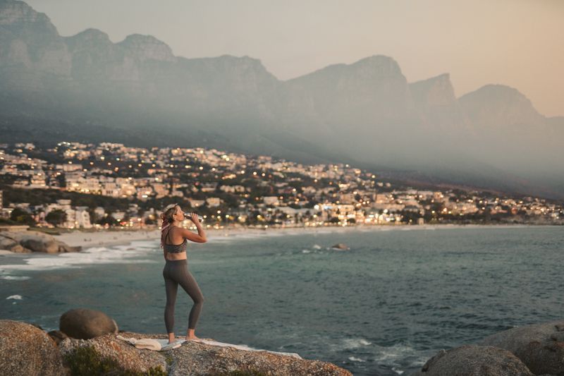 Woman overlooking Camps Bay, Cape Town at sunset, with city lights and mountains.