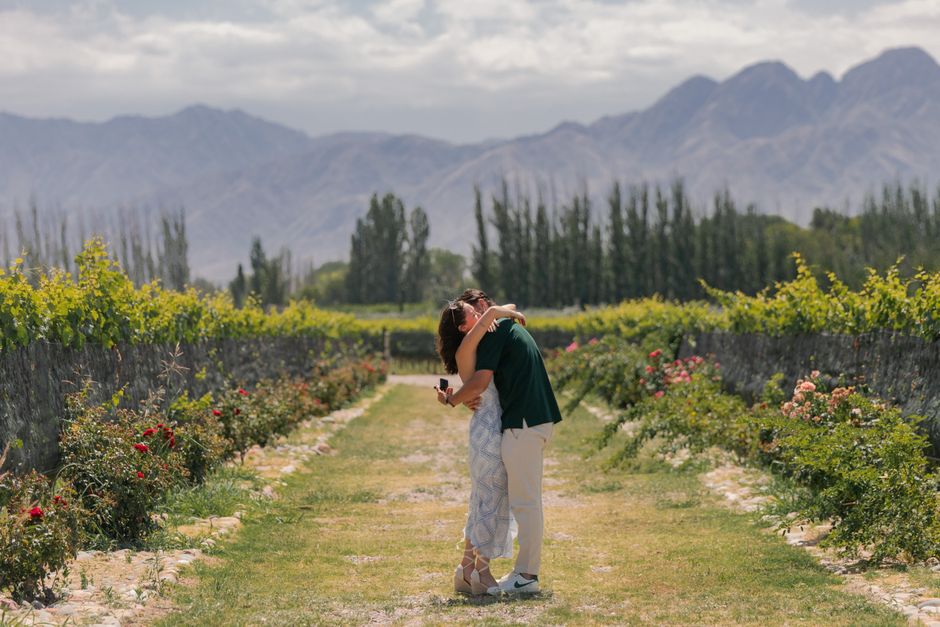 Couple embraces in a picturesque vineyard in Provincia de Mendoza with mountains in the background.