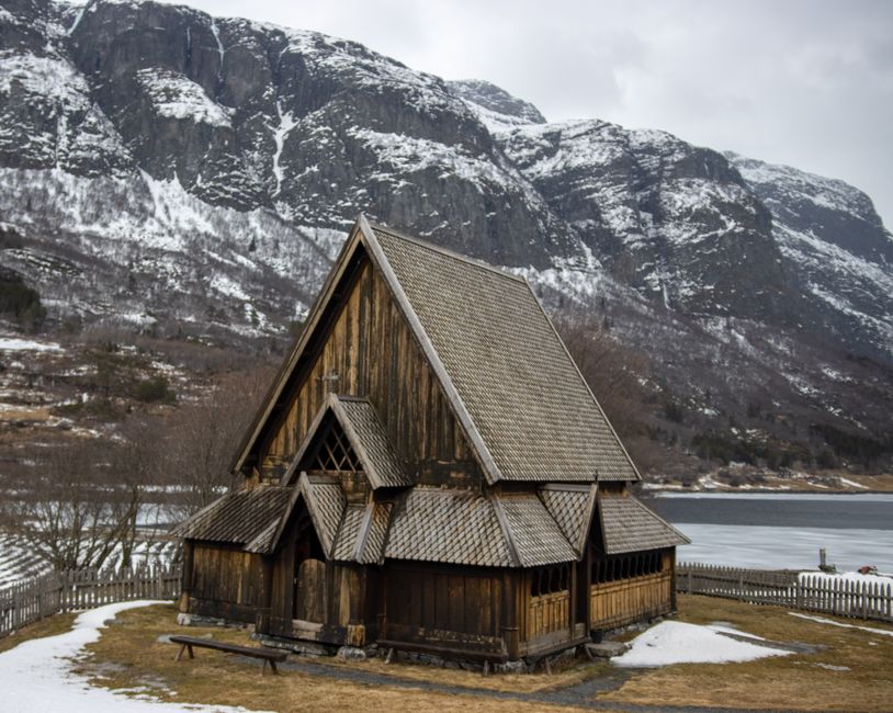 Scenic view of a historic wooden church with snow-covered mountains in Øye, Norway.